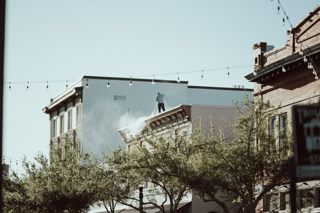 Rooftop worker using pressure washer in a cityscape with urban street below.